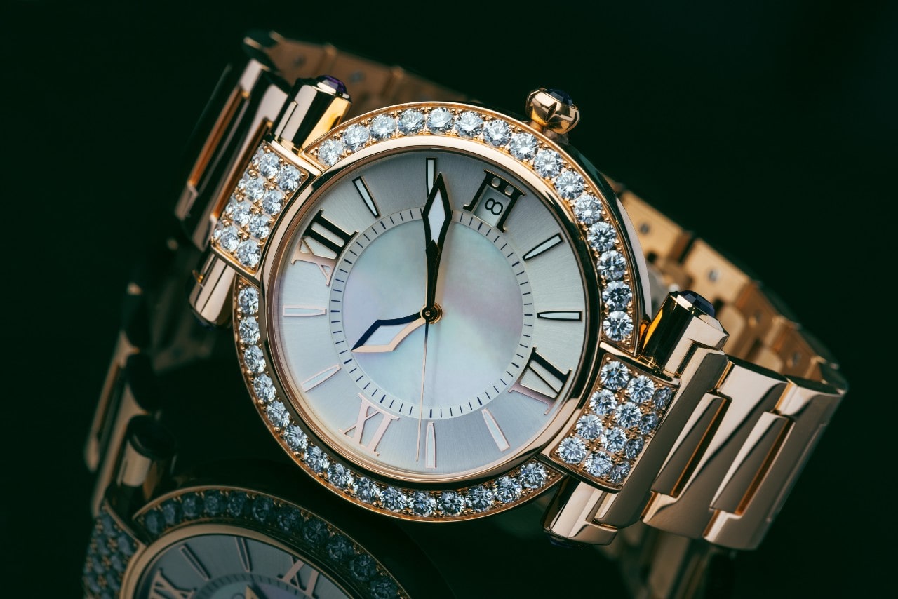 A diamond adorned watch sits on a black reflective surface.