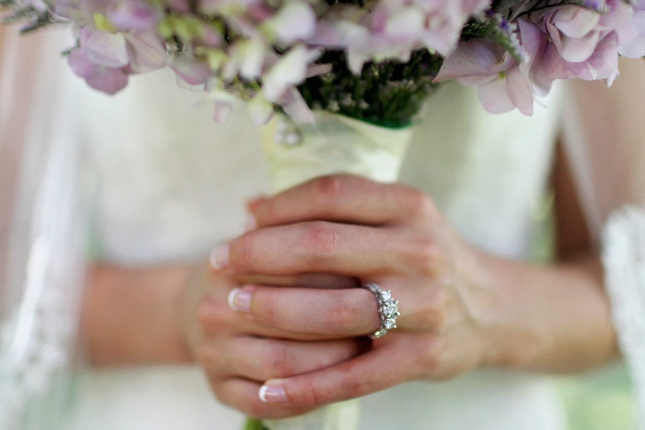 A close-up of a bride’s hands, wearing a three stone engagement ring as she walks down the aisle.