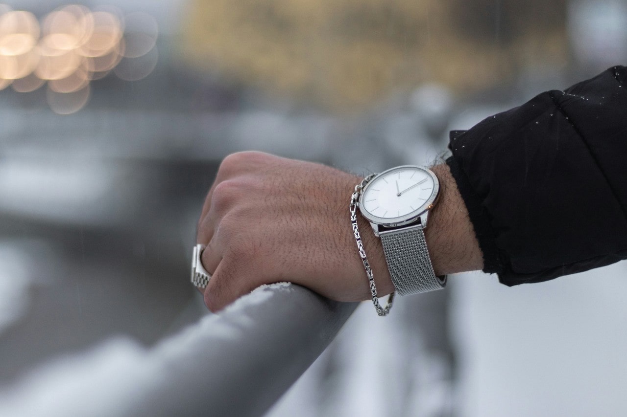 a man’s hand resting against a rail wearing a wrist watch and other jewelry