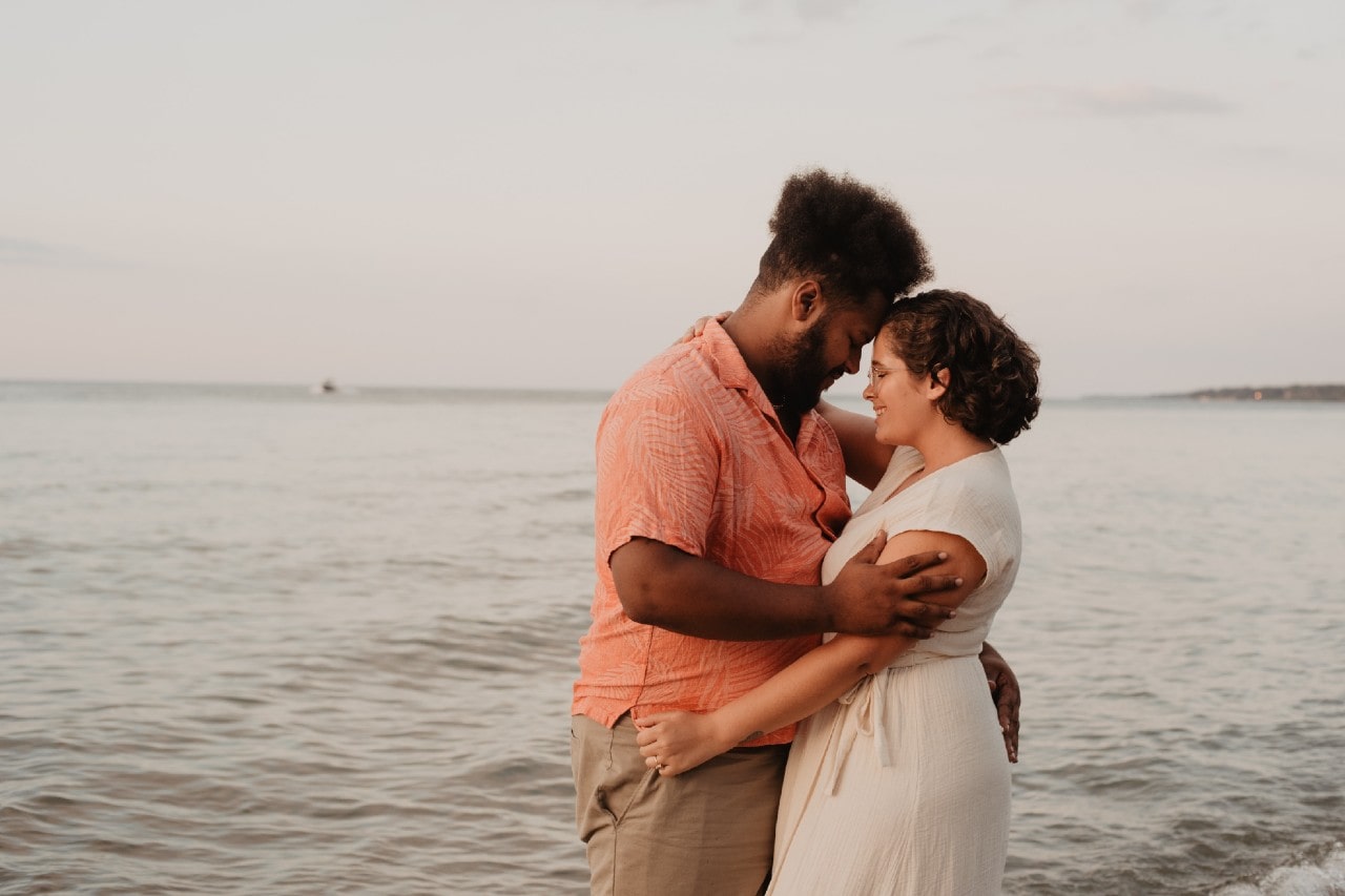 Man and woman hugging in front of a body of water.