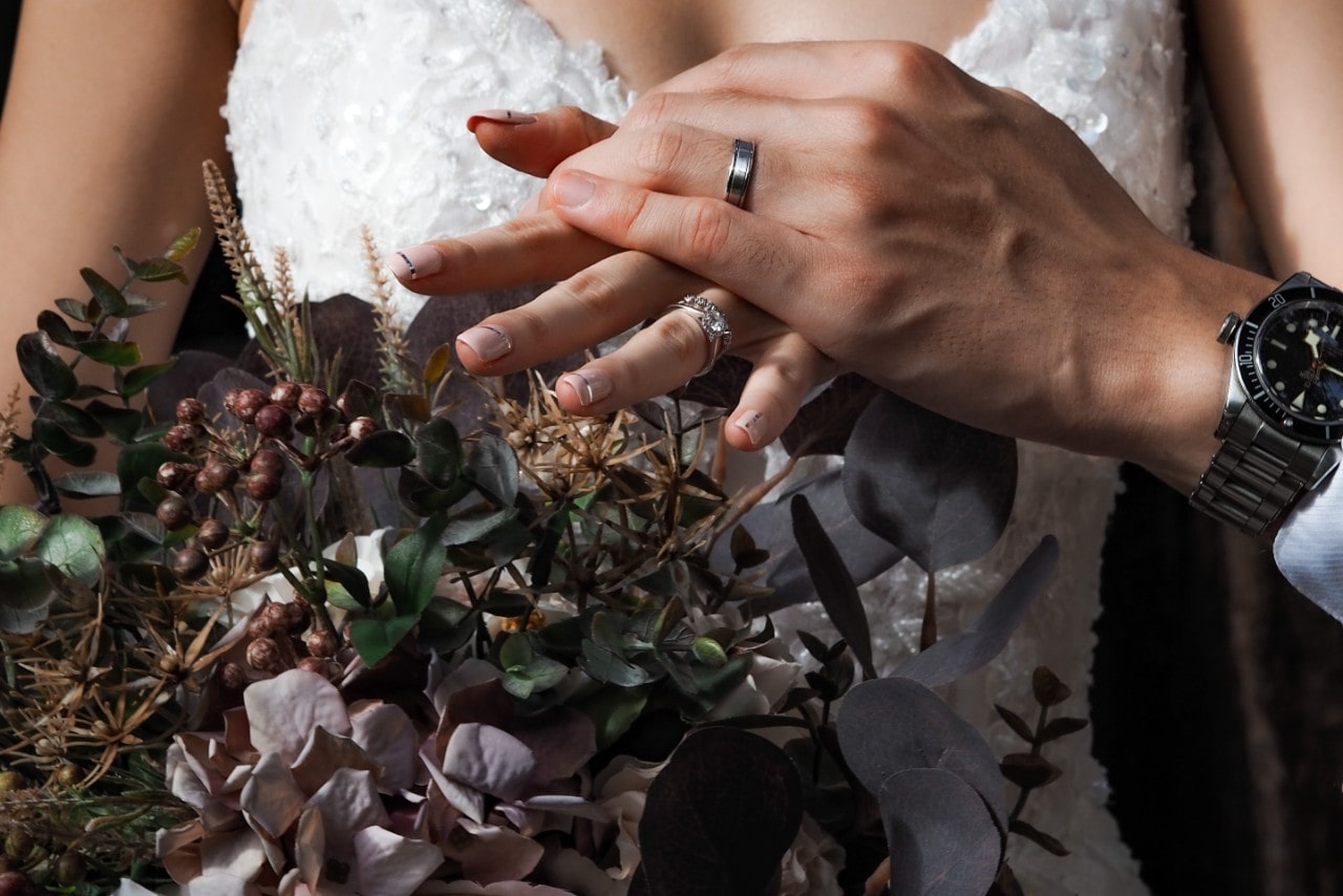 A bride and groom hold hands with their bridal jewelry visible.