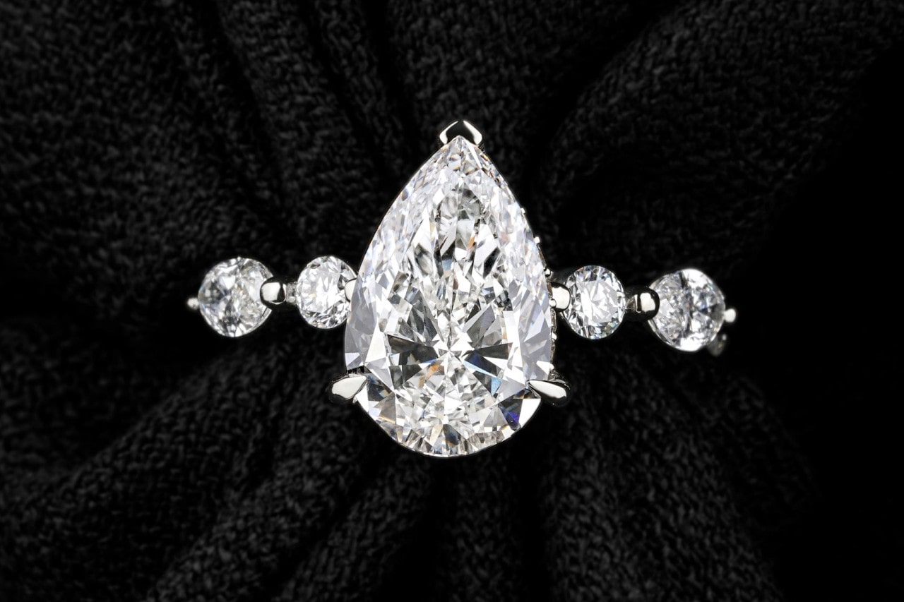 close up image of a pear shape engagement ring with round side stones