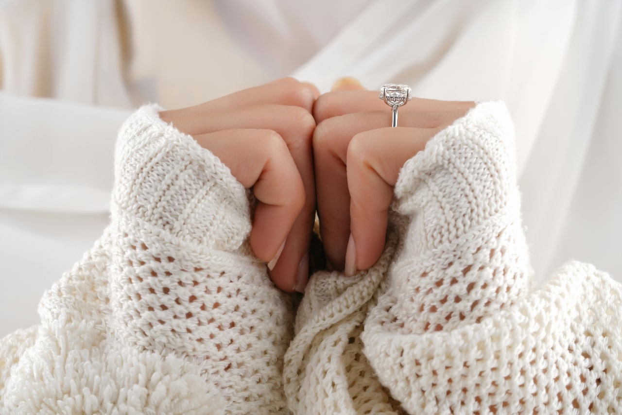 A woman’s hands pressed together, accented by white sweater sleeves and a white gold engagement ring.