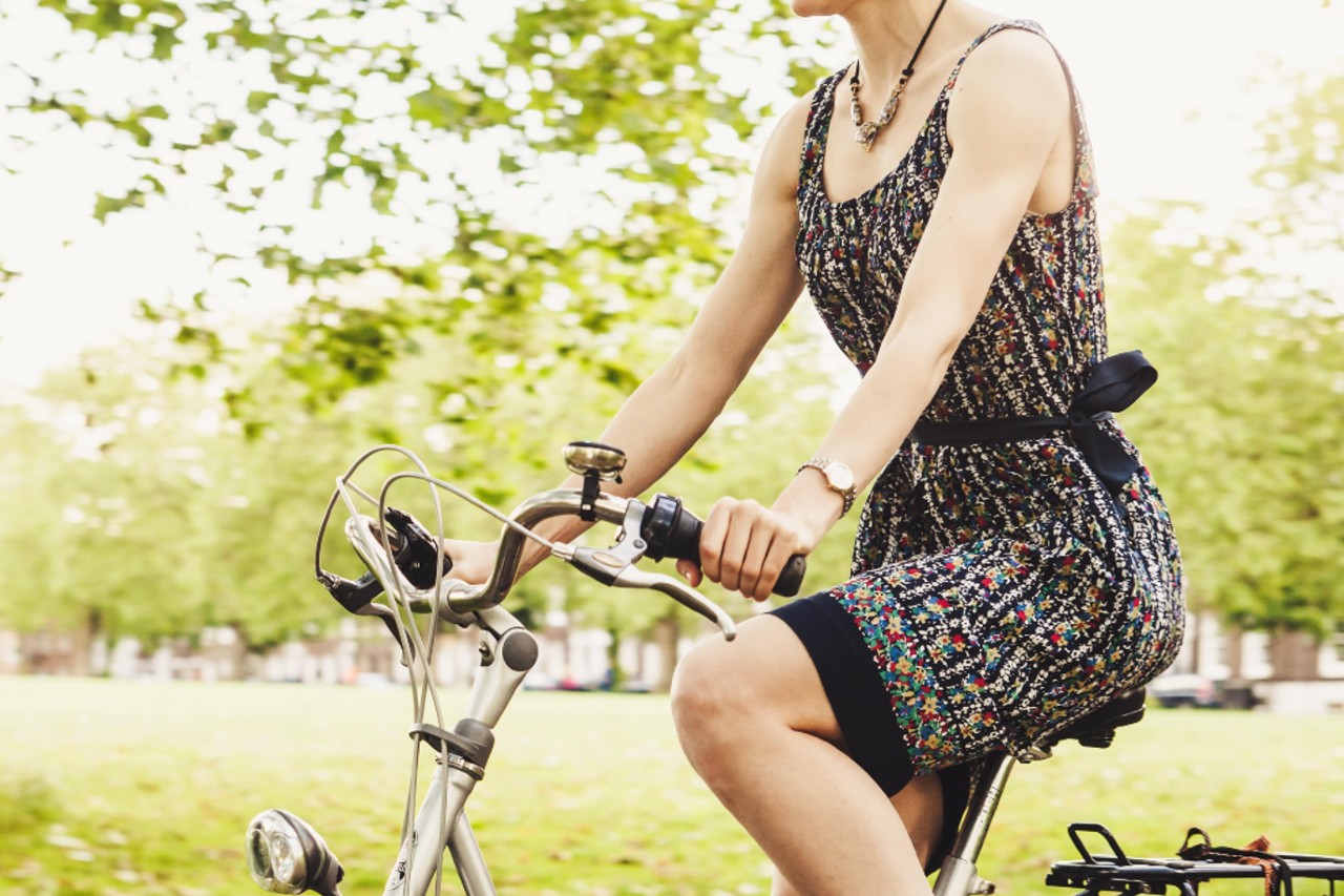 A young woman wearing a simple wrist watch, riding her bicycle through a park.