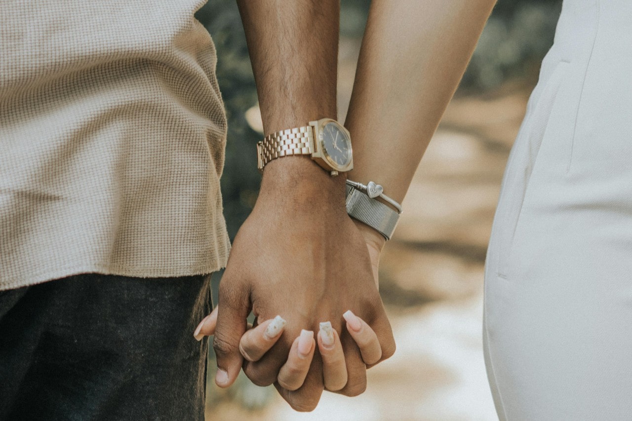 a close-up image of a couple holding hands, the man wearing a simple gold dress watch