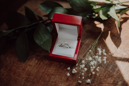 an engagement ring in a red ring box sitting on a table next to baby’s breath and leaves