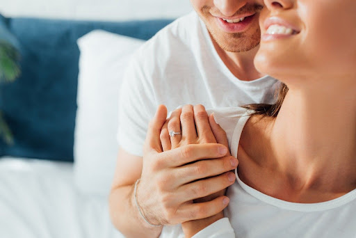 a man and woman sitting up in bed displaying her engagement ring