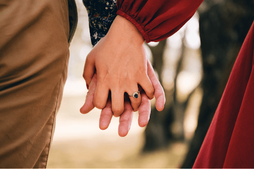 a man and woman holding hands with a sapphire engagement ring on her finger