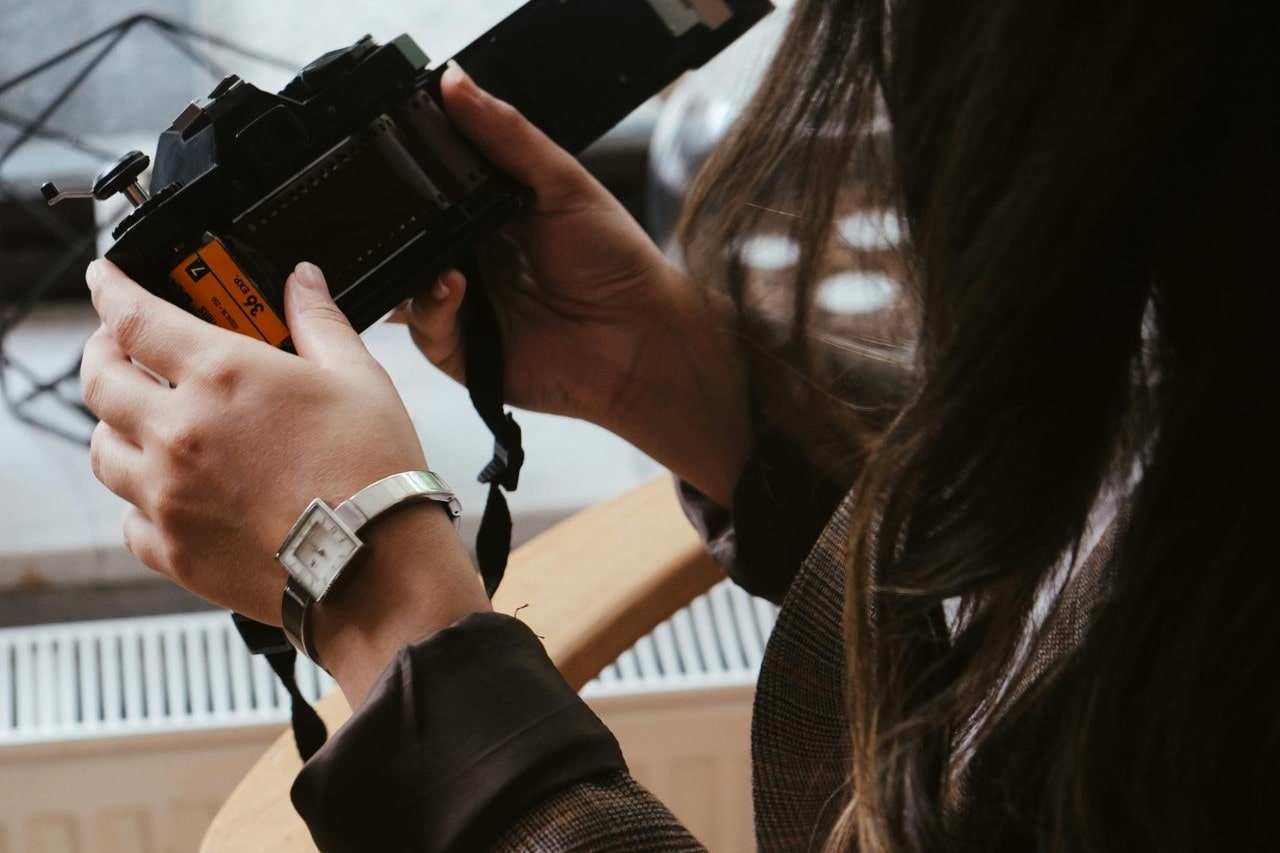 A woman holding a vintage camera and wearing a watch with a square case.