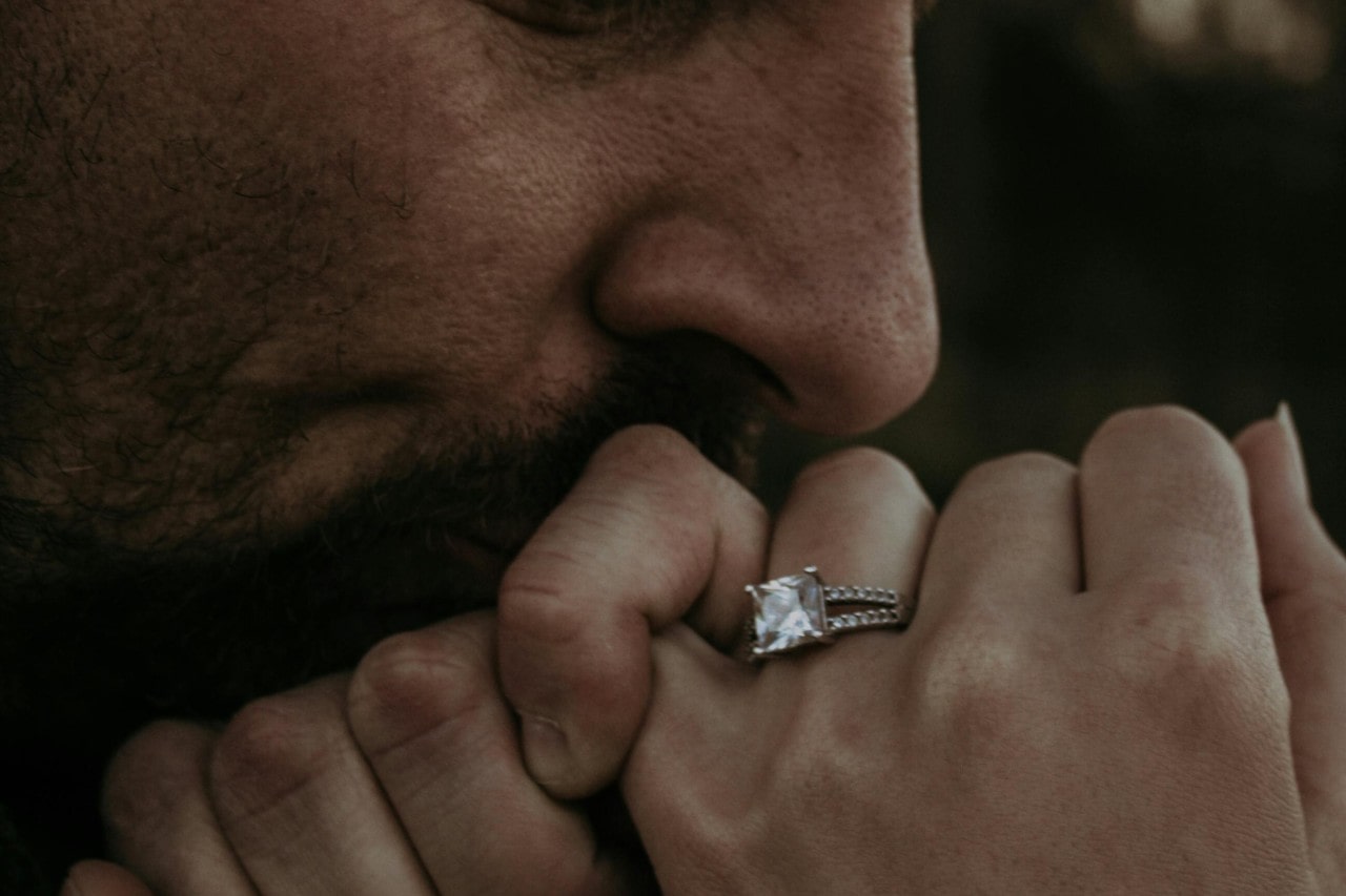 a man kissing a woman’s hand who is wearing a princess cut engagement ring