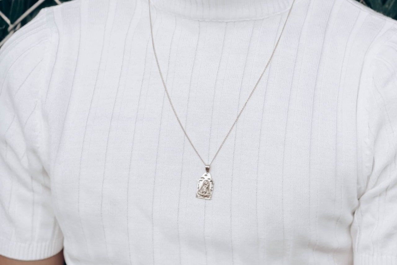 close up image of a man’s chest wearing a white shirt and a silver pendant necklace