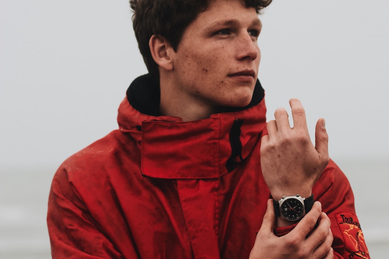 A man in a red raincoat adjusts the watch on his wrist.