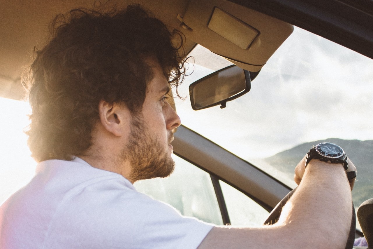 A casual young man drives through the mountainside wearing a sporty watch.