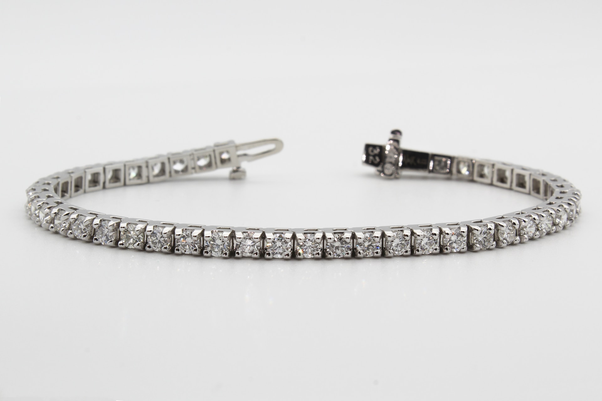 a white gold tennis bracelet set with round cut diamonds on a white surface