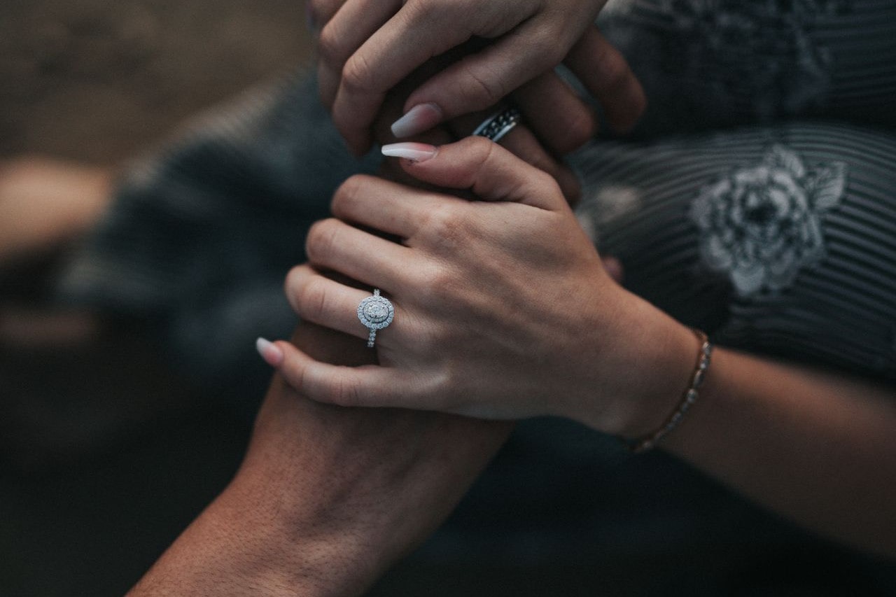 Oval cut diamond ring with a halo setting, worn by a lady holding hands with her husband.