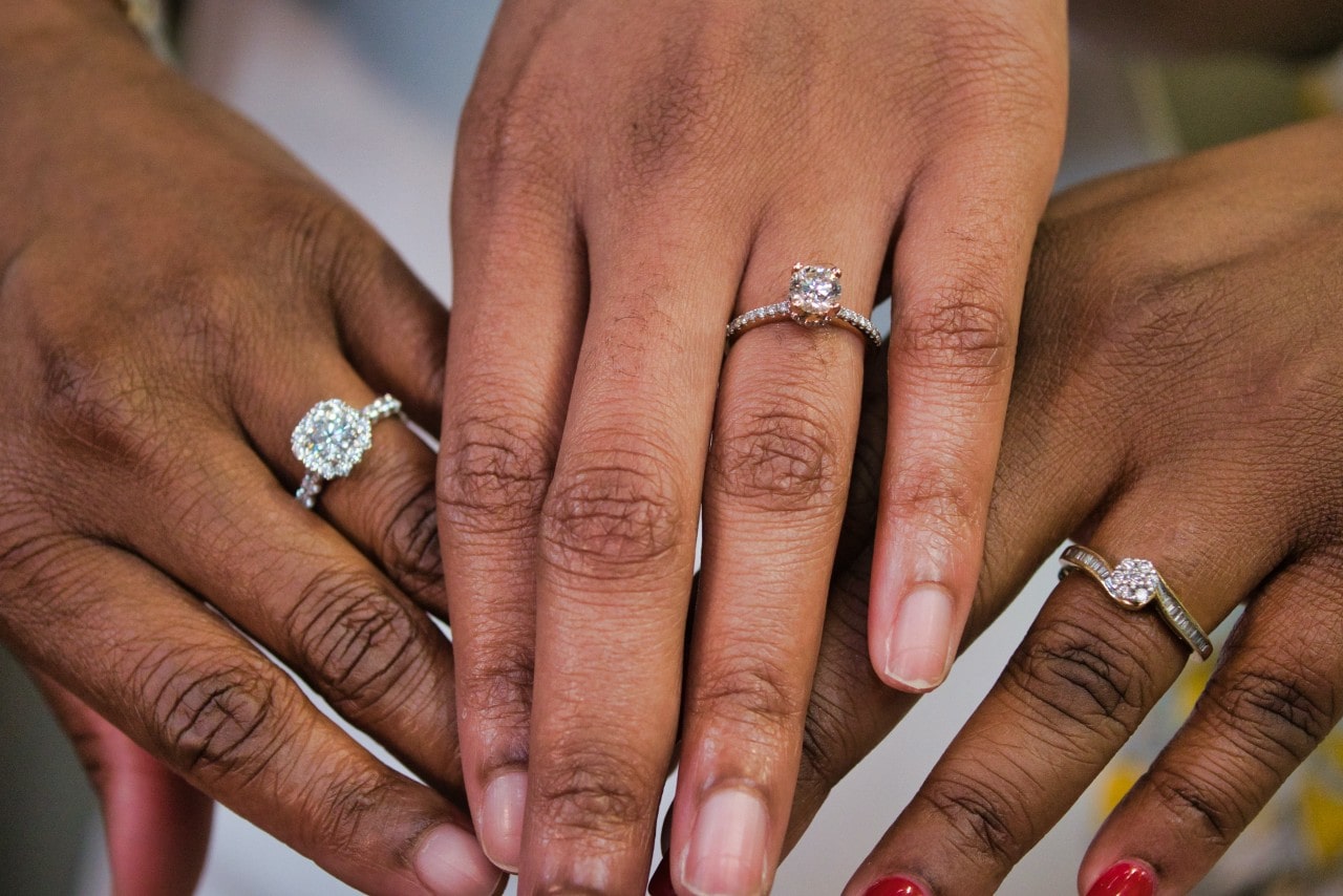 A close-up of three hands, each wearing a stunning engagement ring.