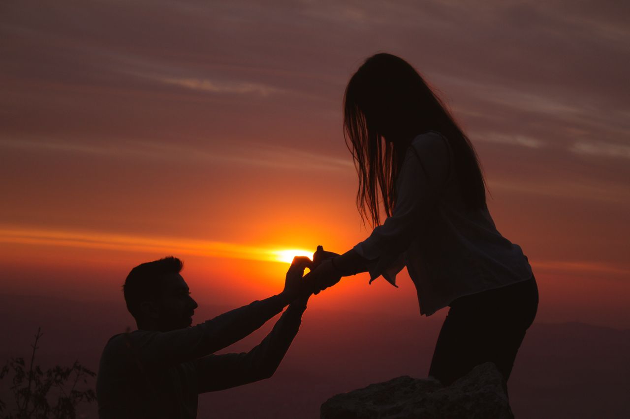 A dramatic shot of a man proposing to his partner, as they’re both backlit by a stunning sunset.