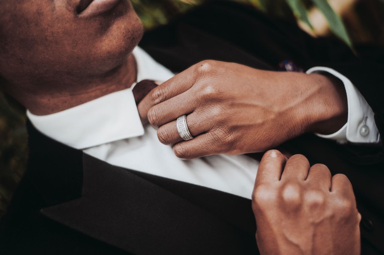 A groom fixing his tie with white gold wedding band on his hand