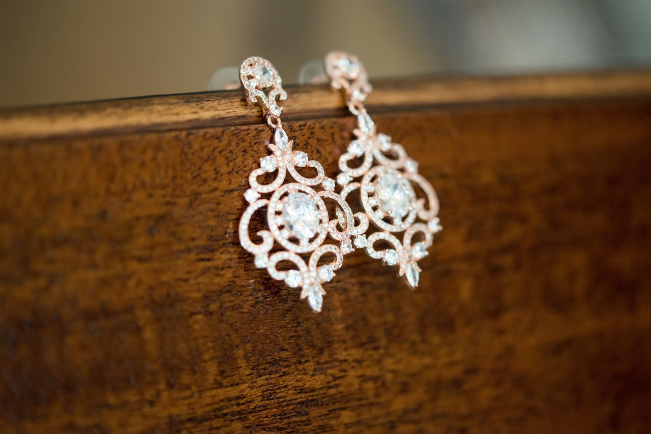 Ornate gold and diamond earrings delicately displayed on a wooden vanity front.