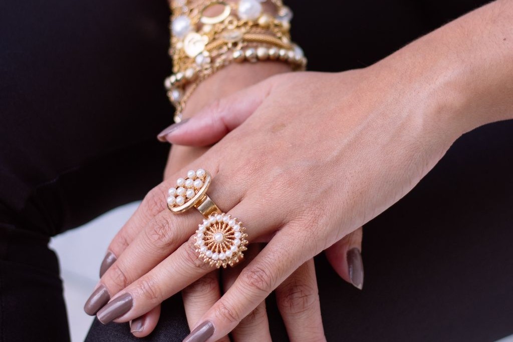 A close-up of a woman’s hands, adorned with many gold rings and bracelets.