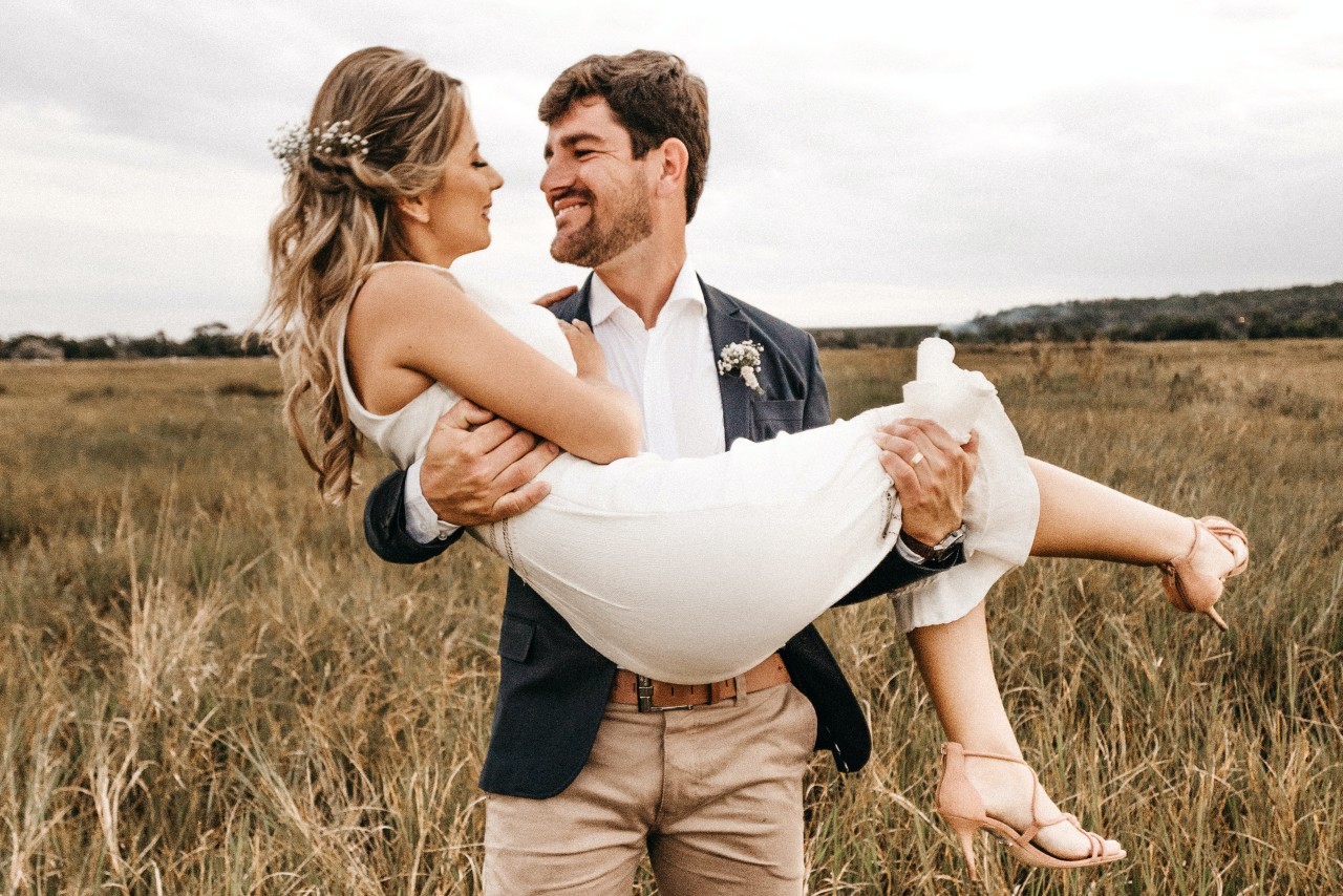 a man holding a bride standing outside in a field