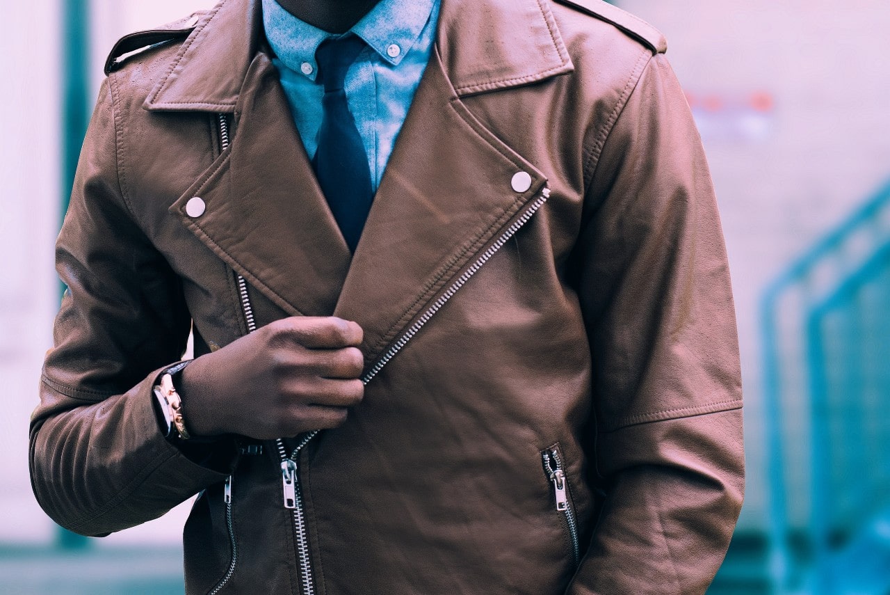 a man in a brown leather jacket wears a vintage watch.